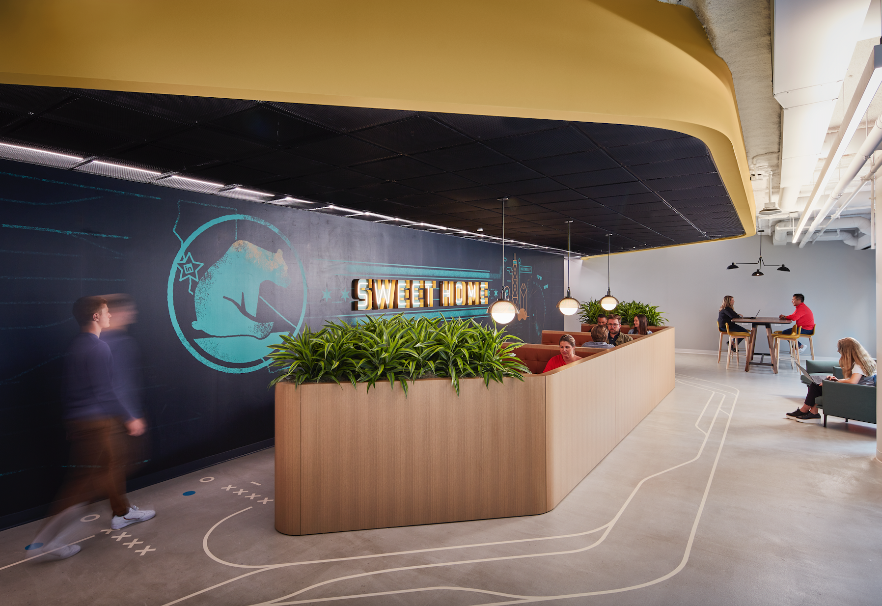 A group of people are sitting at tables in a room with a sign that says sweet home.