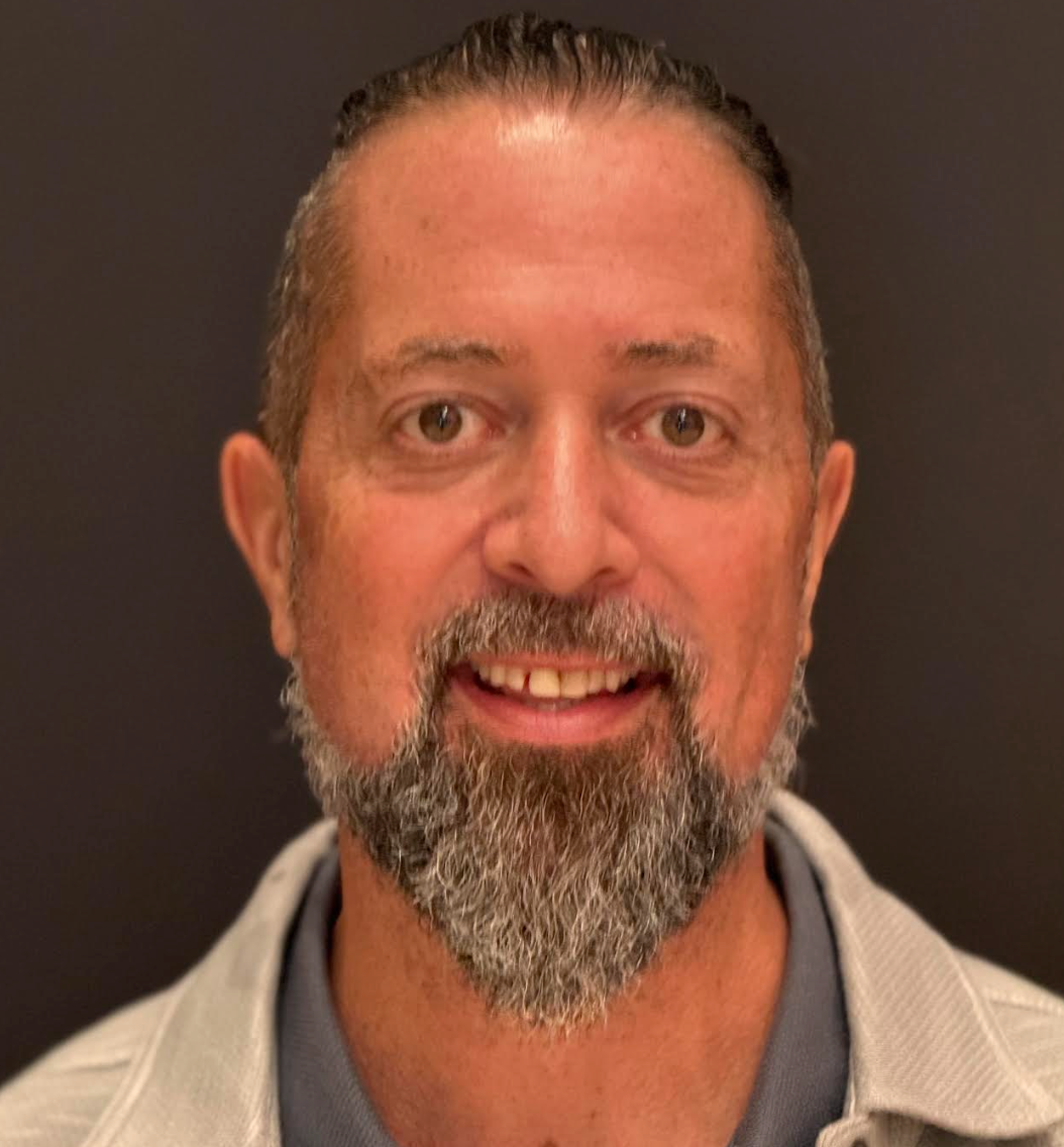 A man in a suit and white shirt is smiling for the camera.