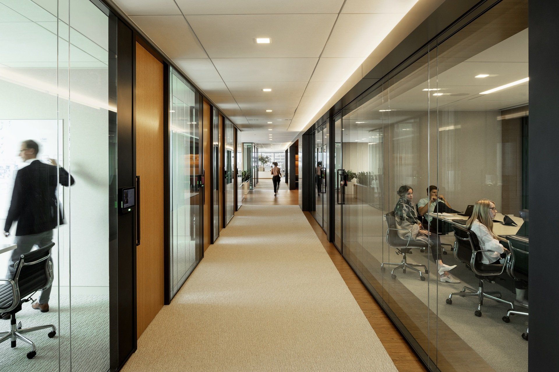 A long hallway with glass walls leading to a conference room.