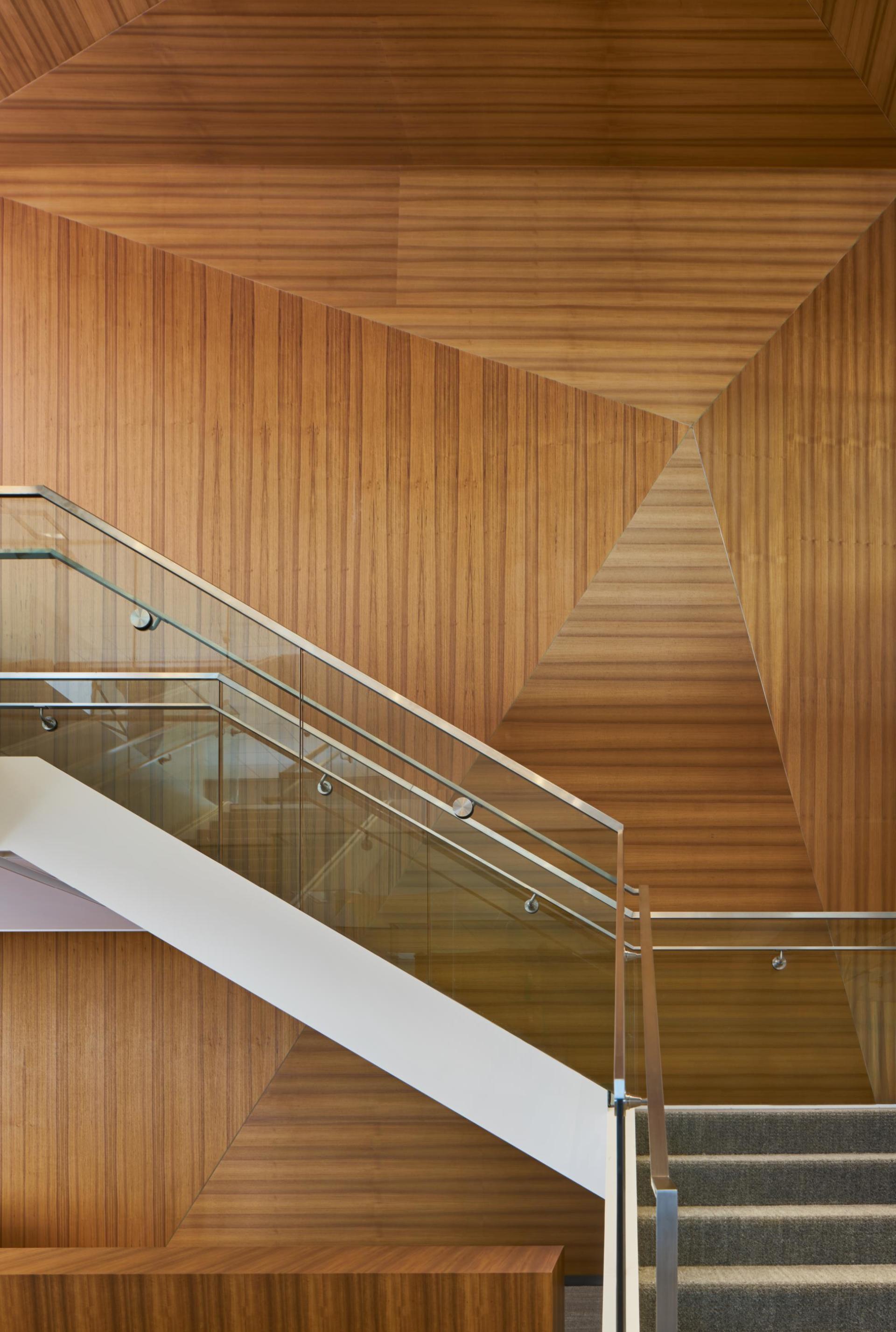 A staircase with a wooden wall and a glass railing.