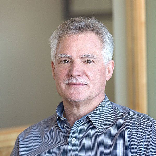 A man with gray hair and a mustache is wearing a plaid shirt and looking at the camera.