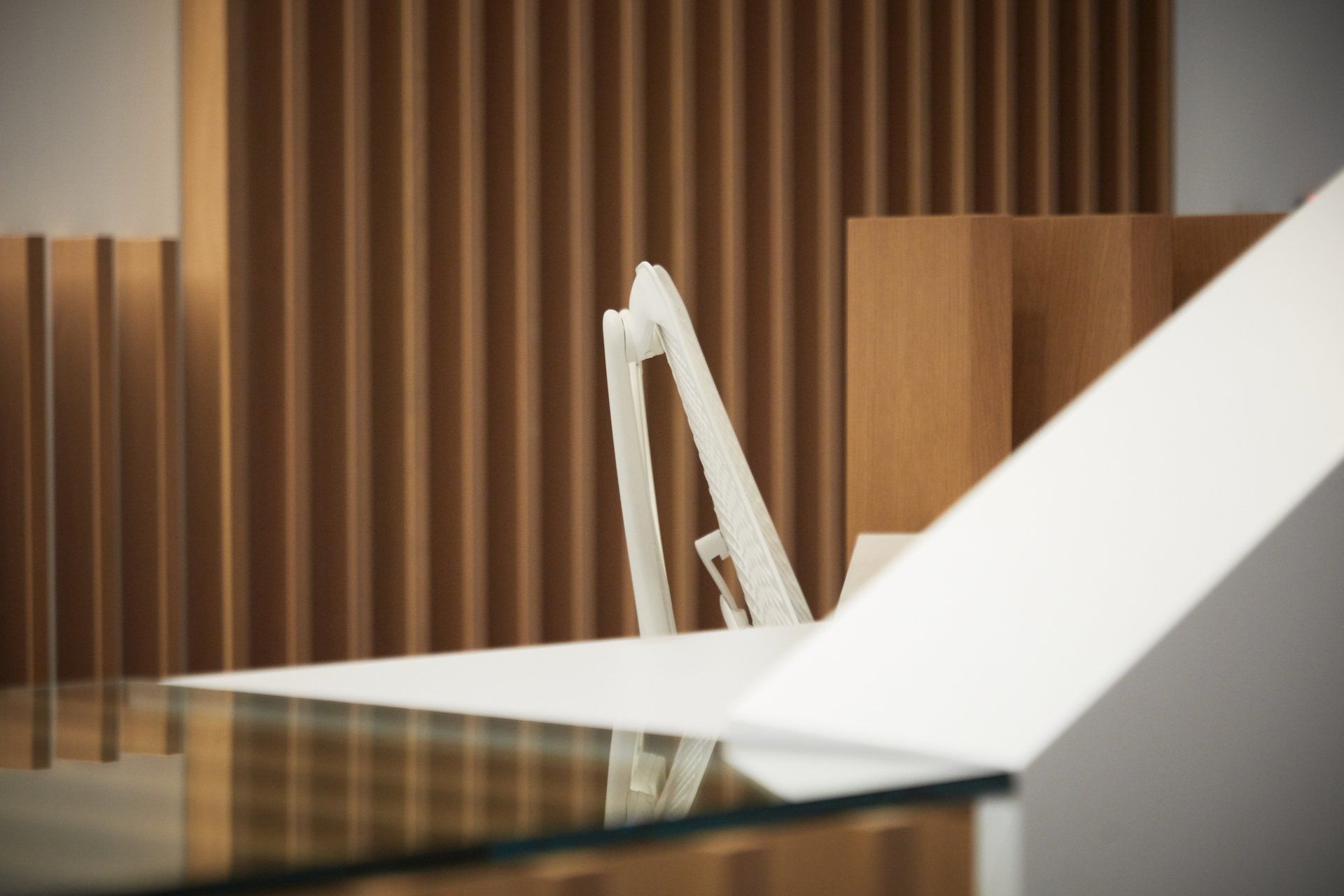 A white chair is sitting on a glass table in front of a wooden wall.