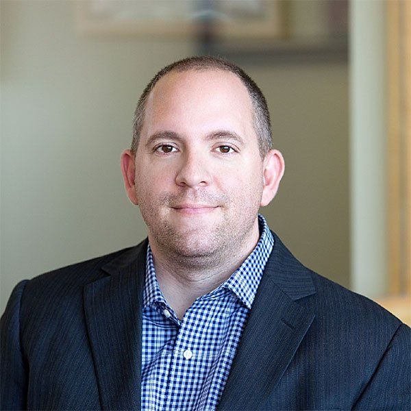 A man in a suit and plaid shirt is smiling for the camera.