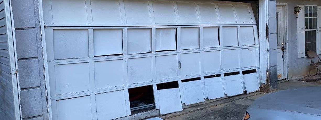 Damaged white garage door with bent panels and openings near the bottom