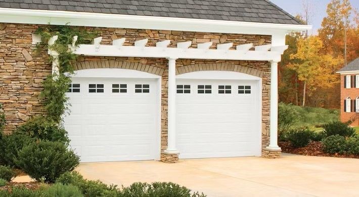 Two white garage doors on a stone house with white trim and a landscaped driveway