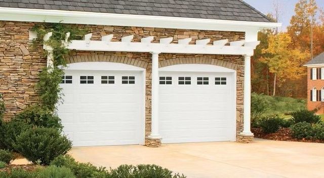 Two white garage doors on a stone house with white trim and a landscaped driveway