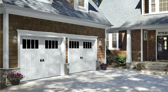 Two-car white garage doors on a stone house with a front porch and landscaped driveway