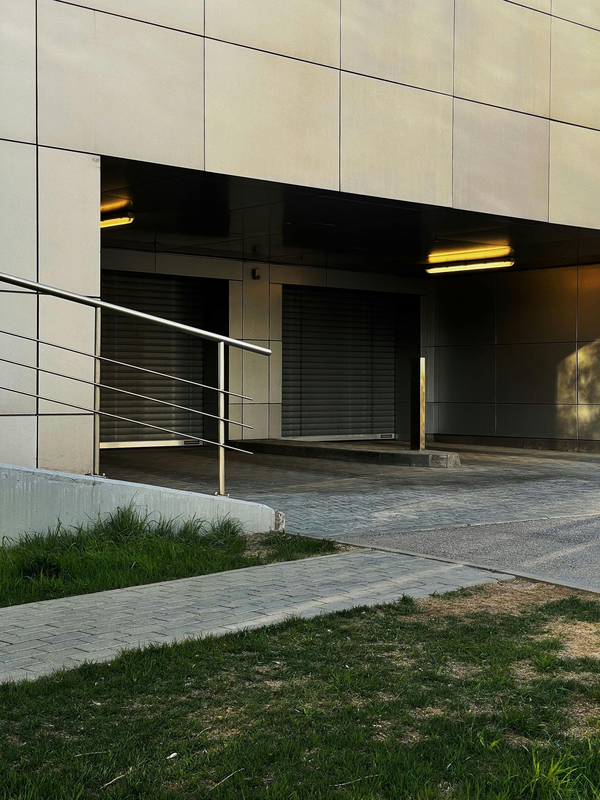 Building entrance with ramp, metal railings, shuttered doorway, and grass in the foreground.