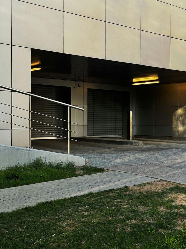 Building entrance with ramp, metal railings, shuttered doorway, and grass in the foreground.