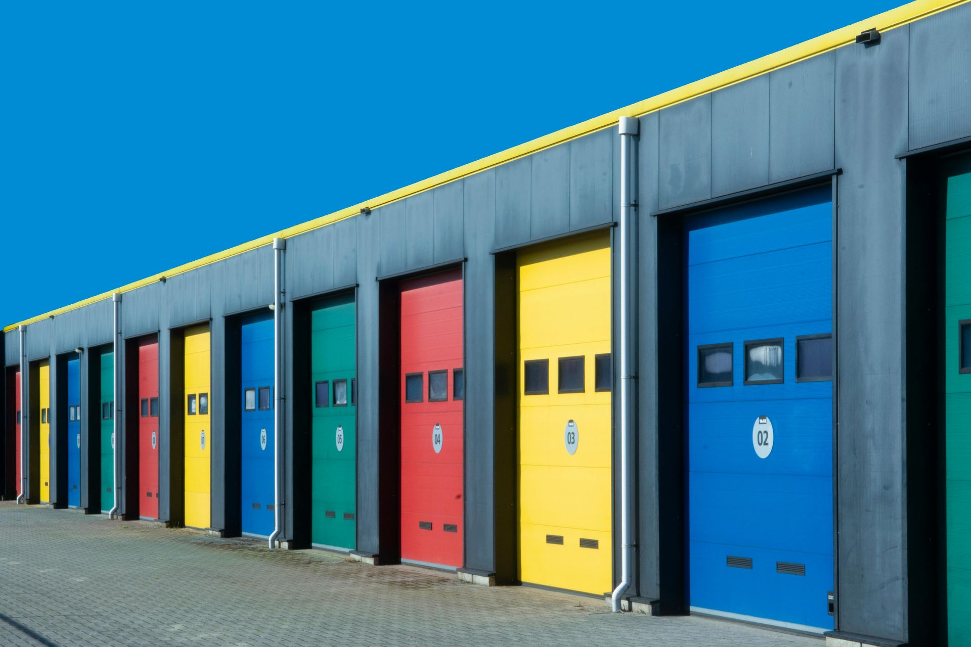 Row of colorful industrial garage doors along a warehouse exterior under a bright blue sky