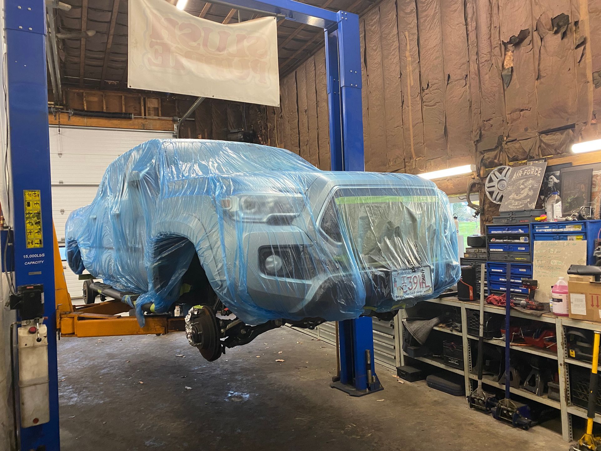 A truck is wrapped in plastic and sitting on a lift in a garage.