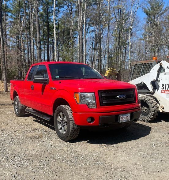 A red ford truck is parked next to a white bobcat skid steer