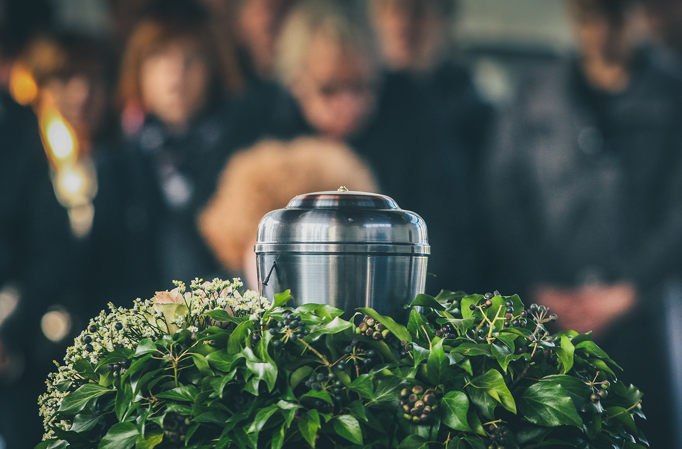 A group of people are standing around a urn at a funeral.