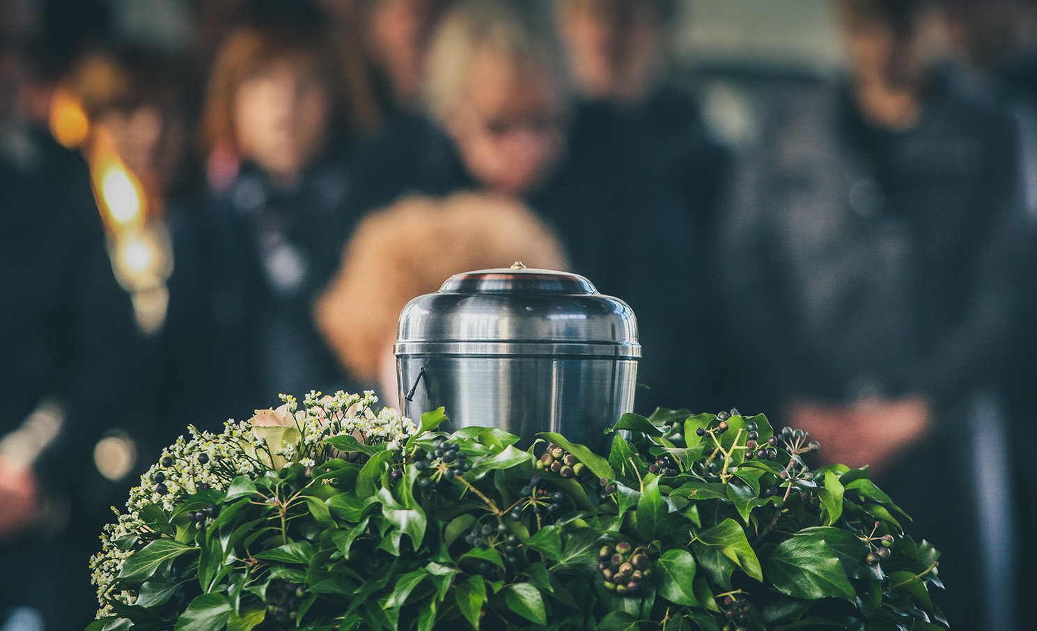 A group of people are standing around a urn at a funeral.