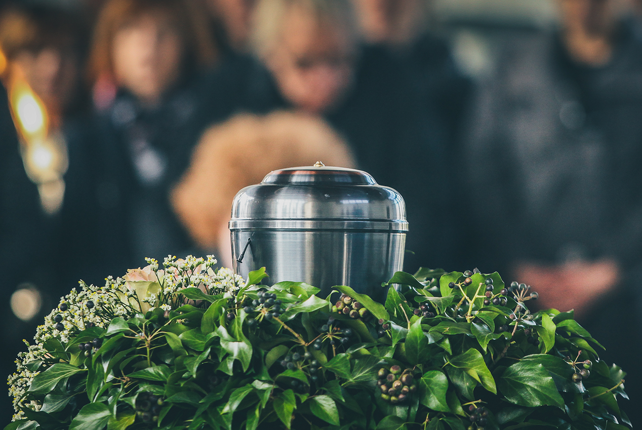 A group of people are standing around a urn at a funeral.