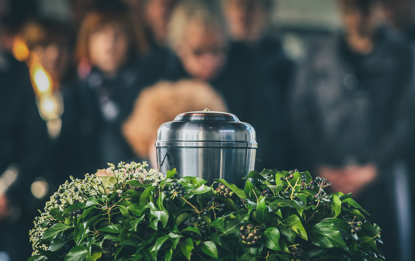 A group of people are standing around a urn at a funeral.