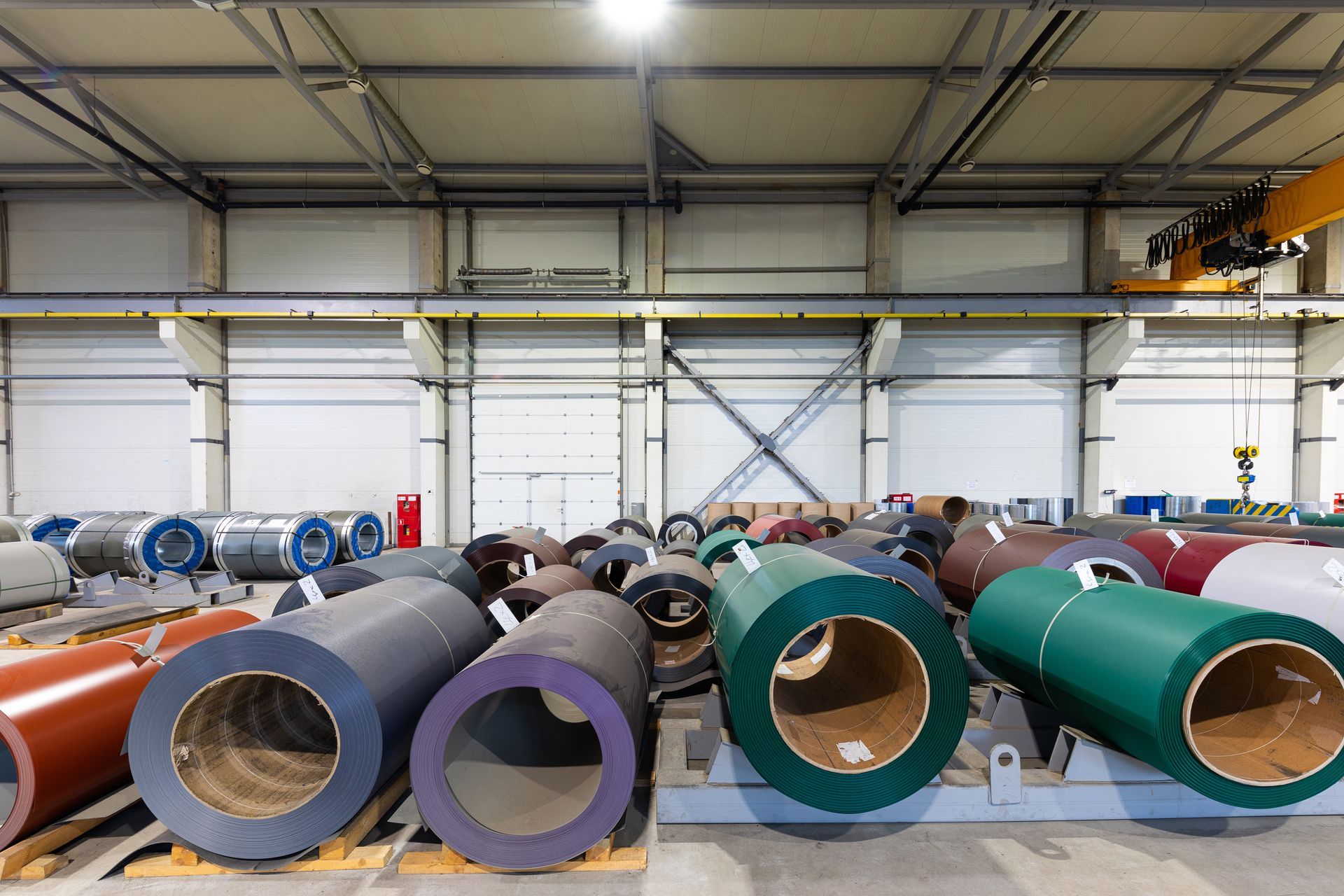 Coils of colored metal sheets stored in a large warehouse.