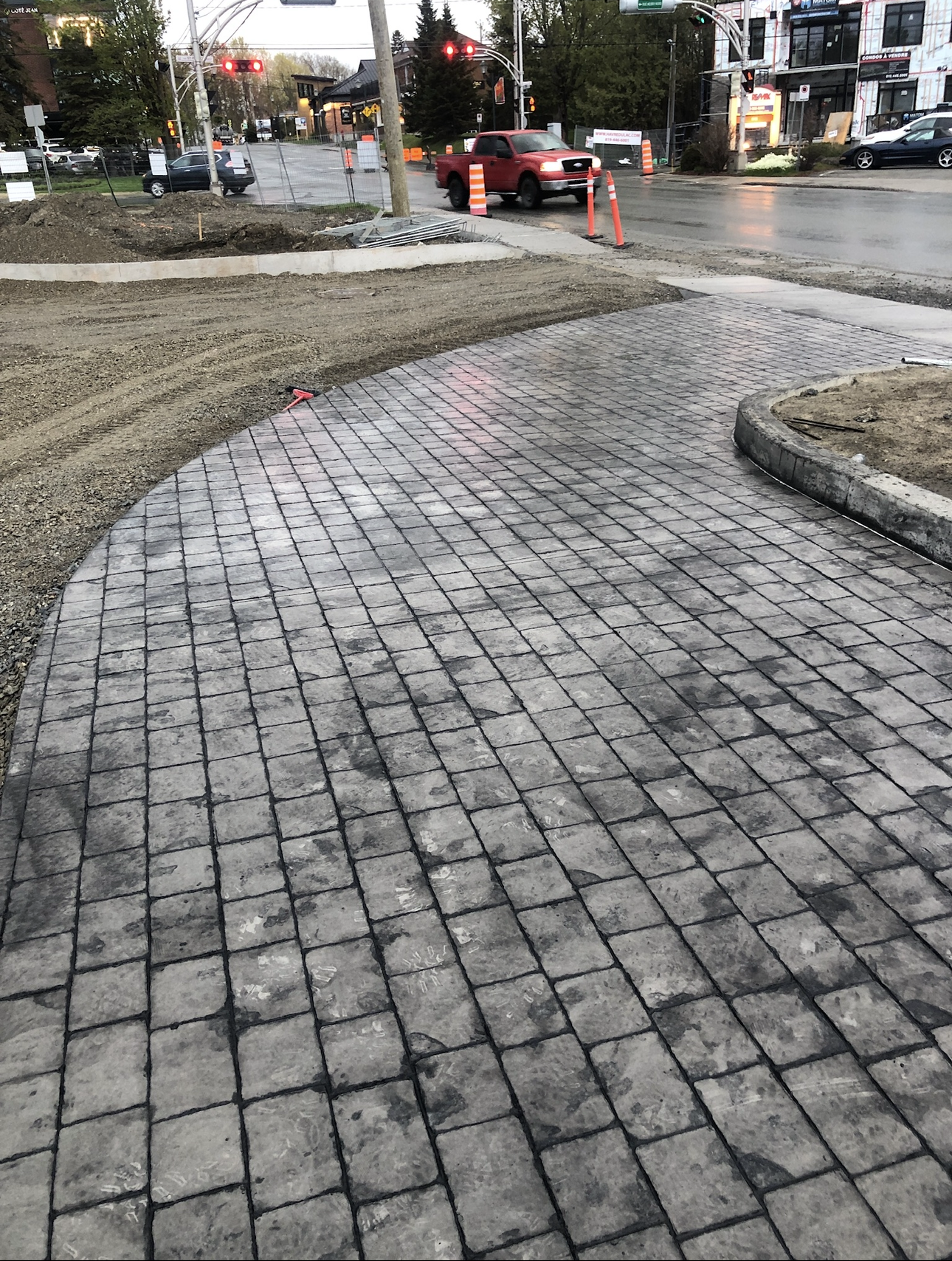 Une voiture rouge roule sur un trottoir en briques à côté d'une rue.