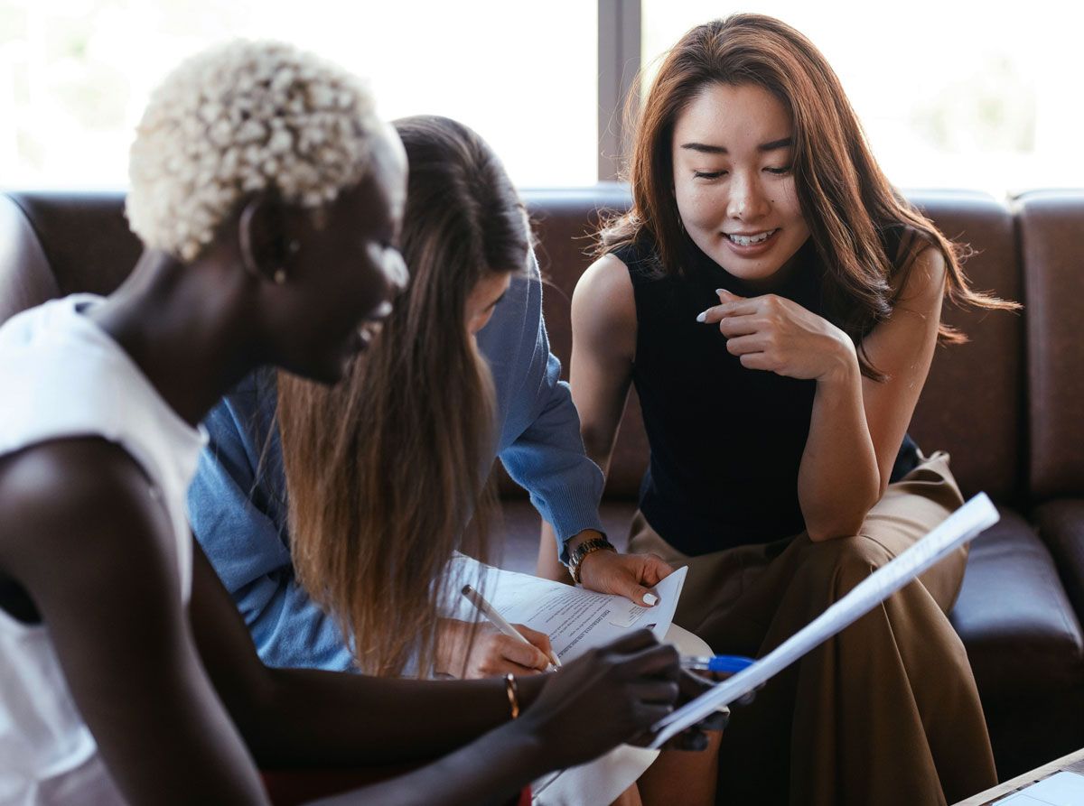 A group of people are sitting on a couch looking at papers.