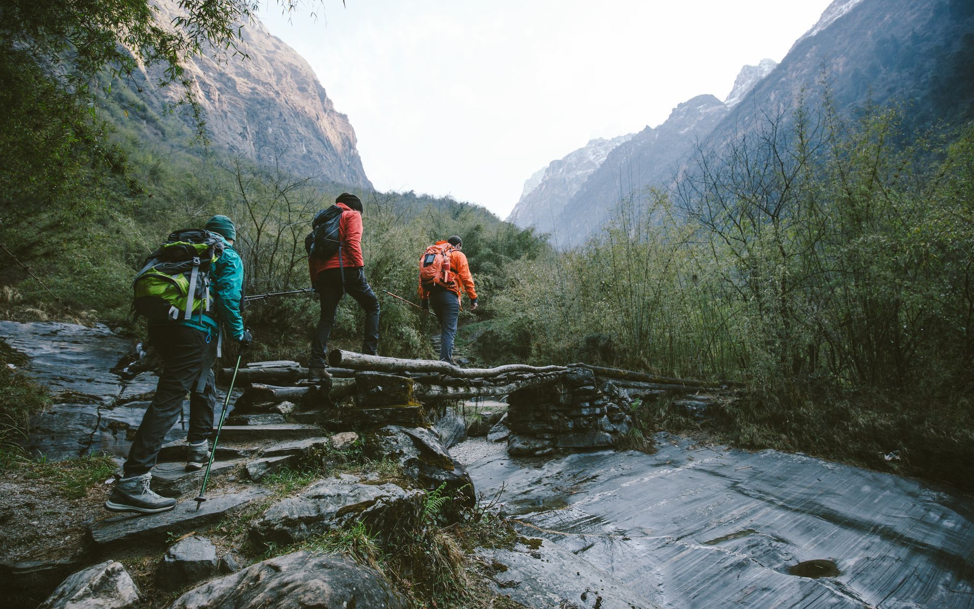 A group of people are walking across a wooden bridge in the mountains.