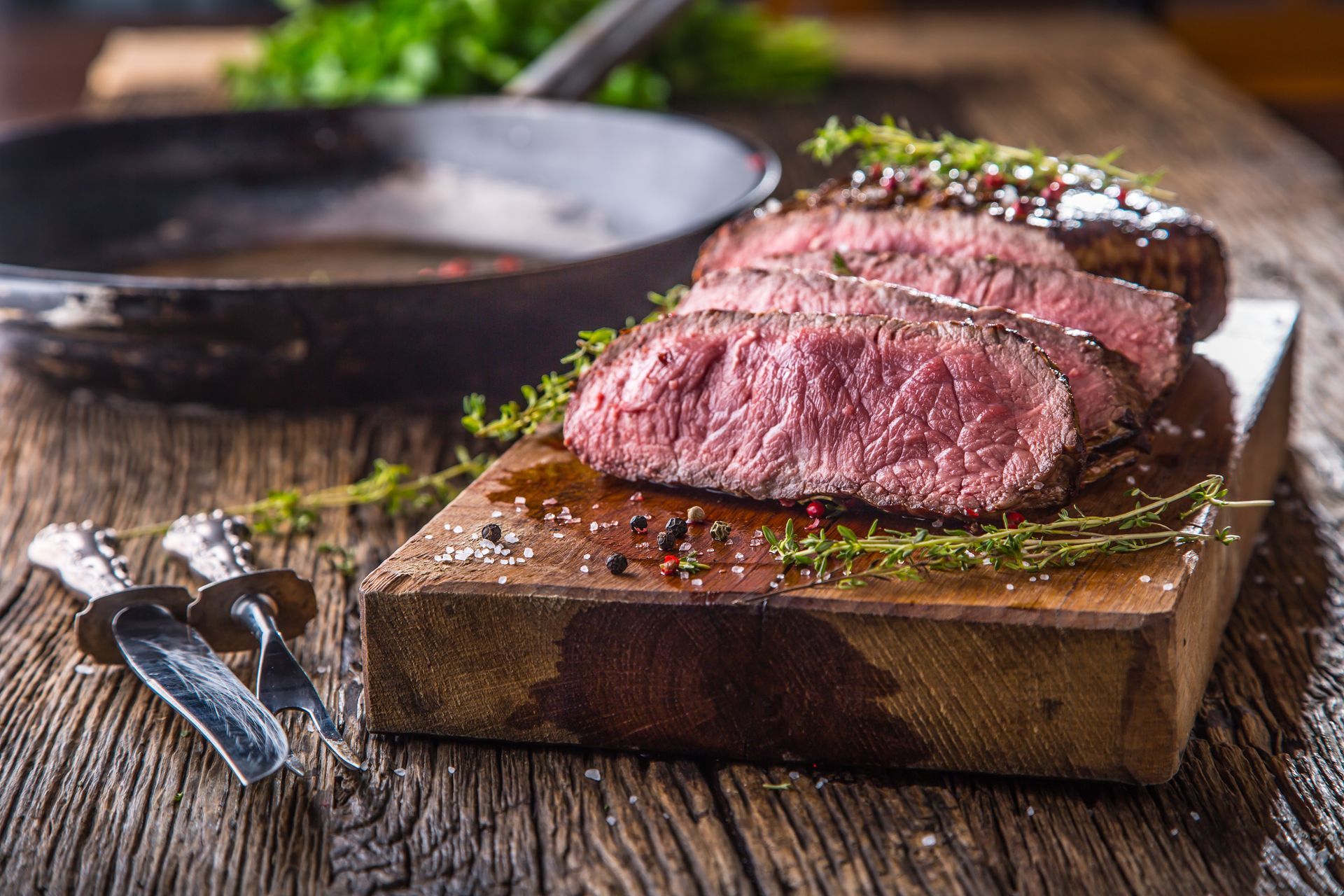 A steak is sitting on a wooden cutting board on a wooden table.