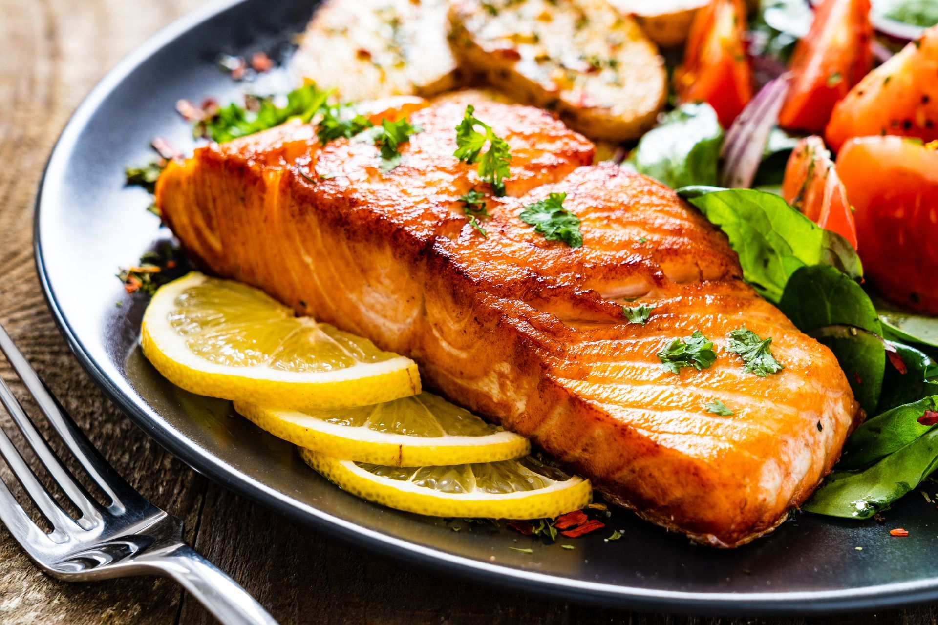 A close up of a plate of food with salmon , lemon slices and vegetables.