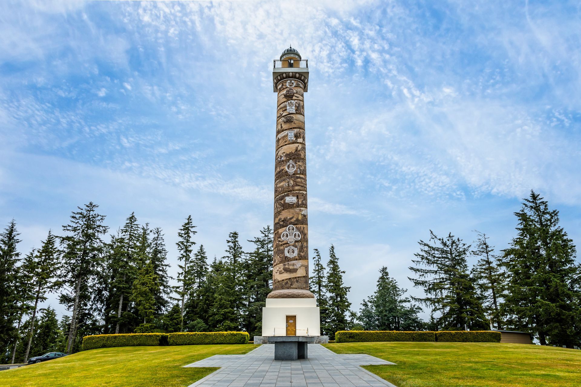 A tall stone tower is in the middle of a grassy field surrounded by trees.