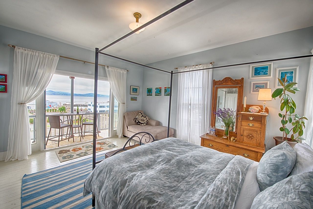 A bedroom with a four poster bed , dresser , mirror and balcony.