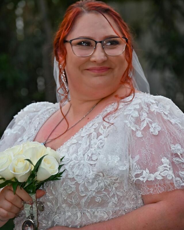 A woman in a wedding dress is holding a bouquet of white roses.