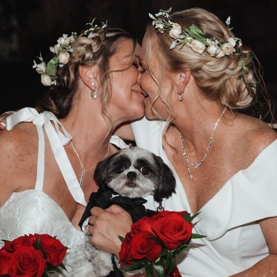 Two women kissing while holding a dog and flowers