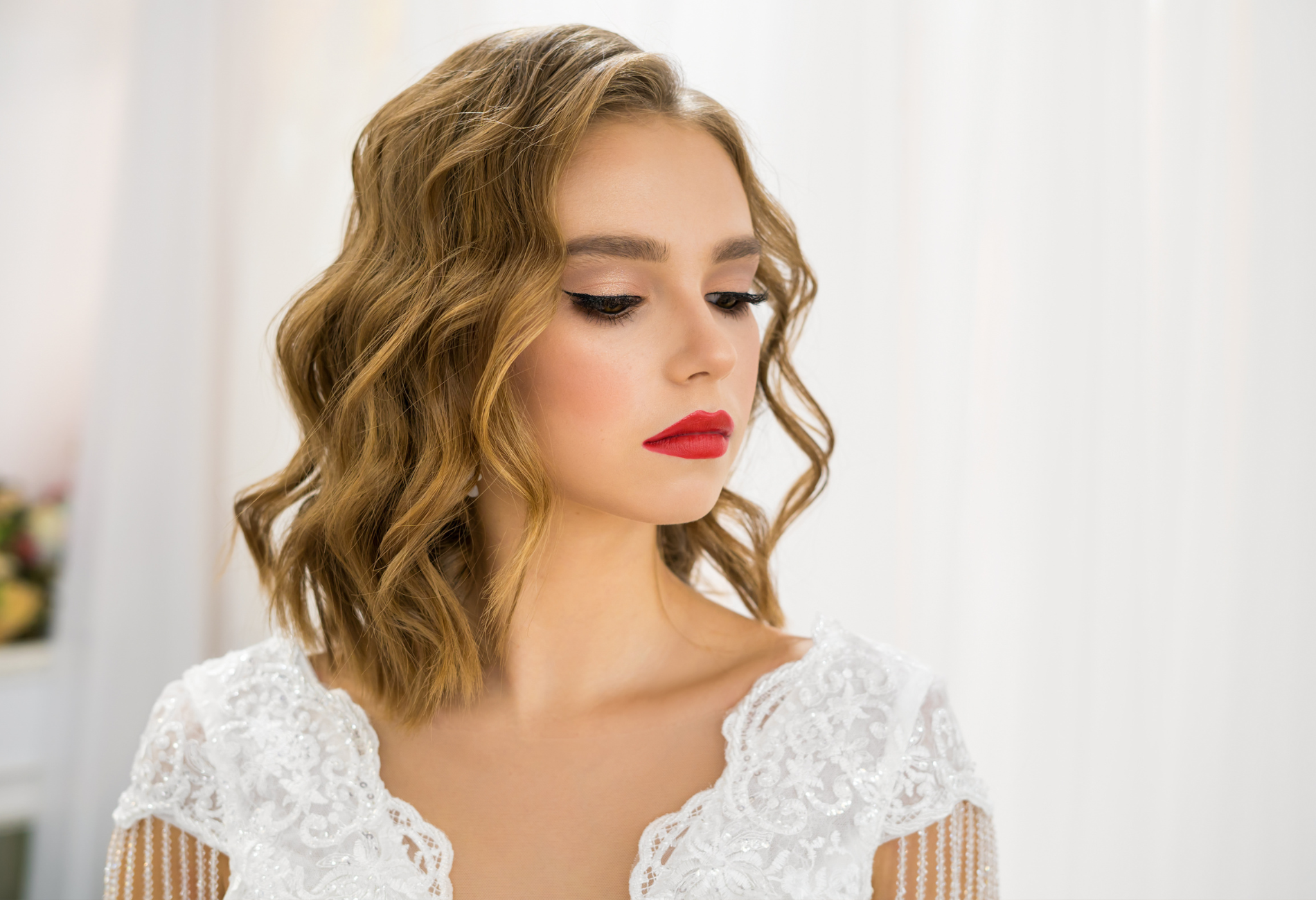The woman is wearing a white lace dress and red lipstick.