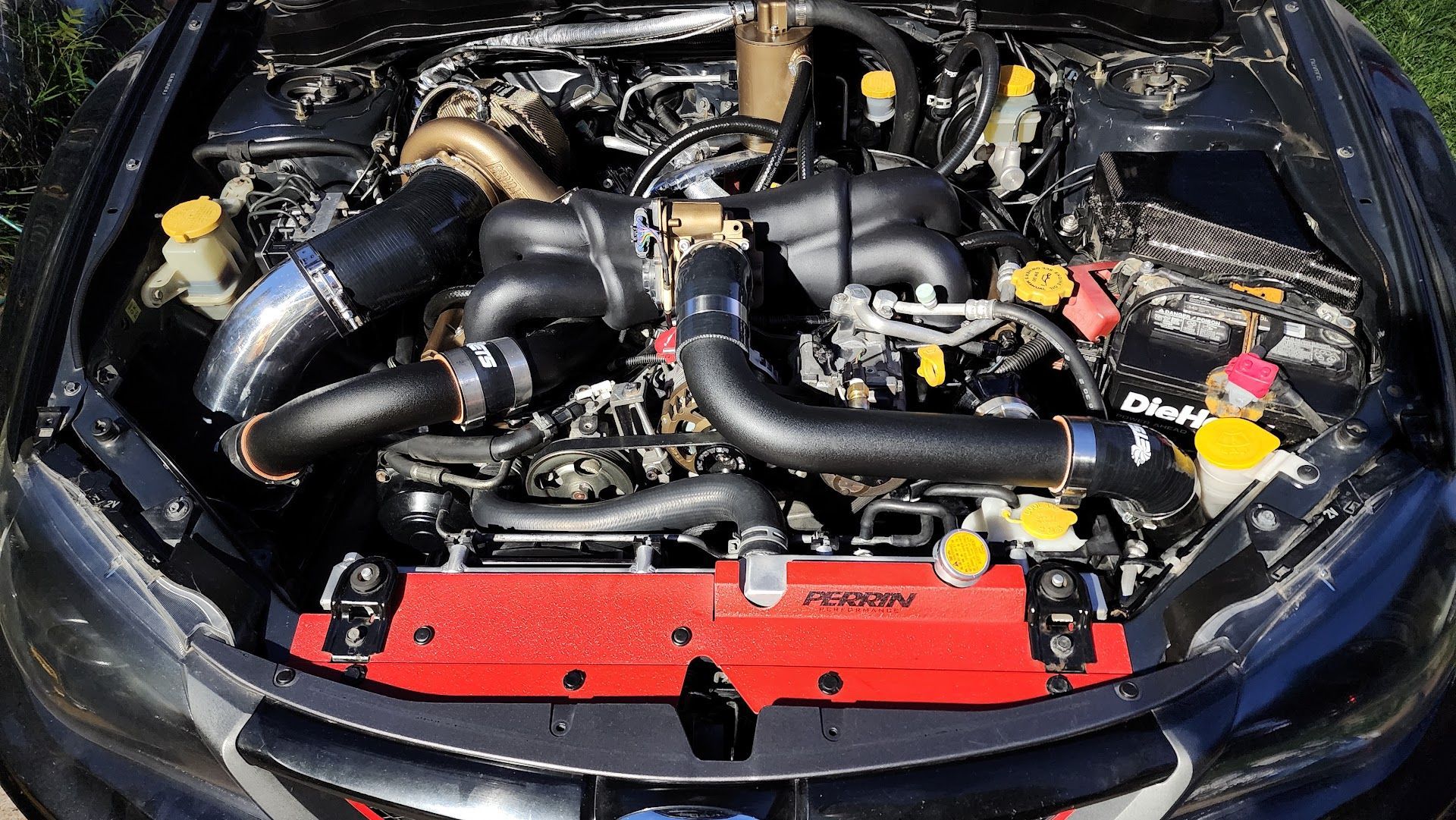 Top-down view of a modified Subaru engine bay with a red radiator, black intake piping, and a large turbocharger. | Teter Auto