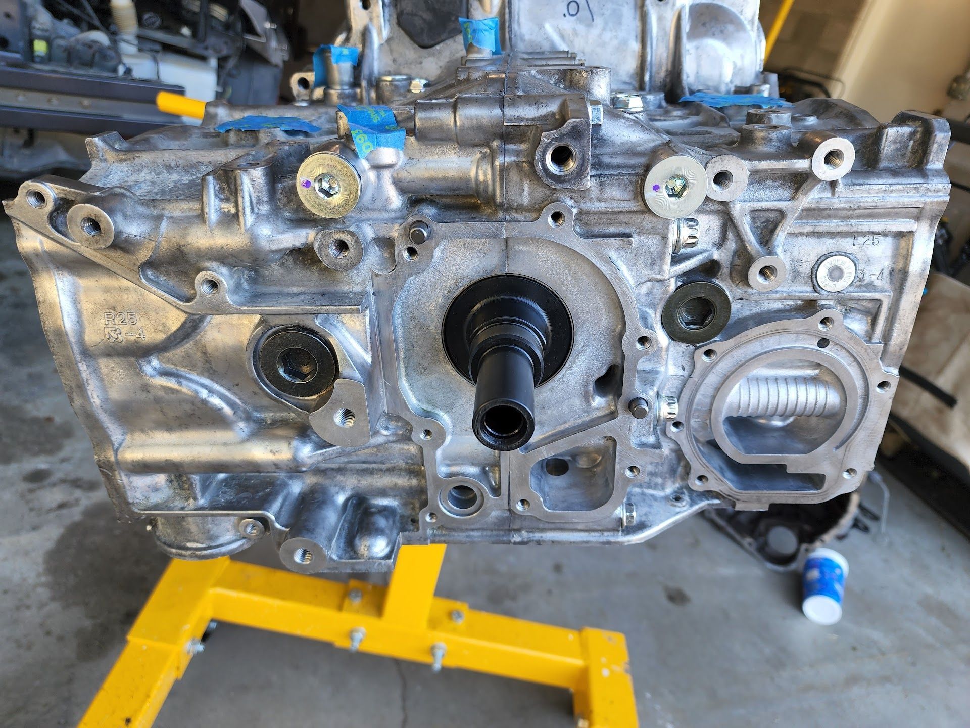 A disassembled aluminum car engine block mounted on a yellow stand in a garage setting. | Teter Auto