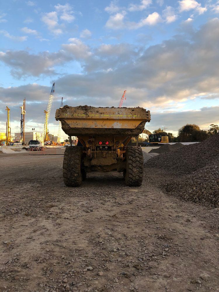 A large yellow dump truck is parked in a dirt field.