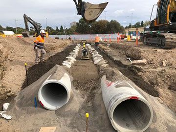 A man is standing next to a pile of pipes in a dirt field.