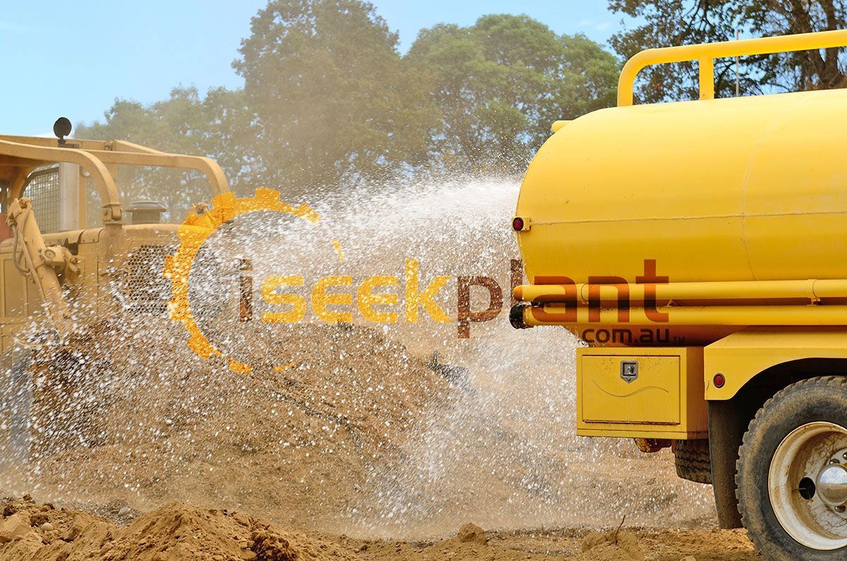 A yellow truck is spraying water on a dirt field