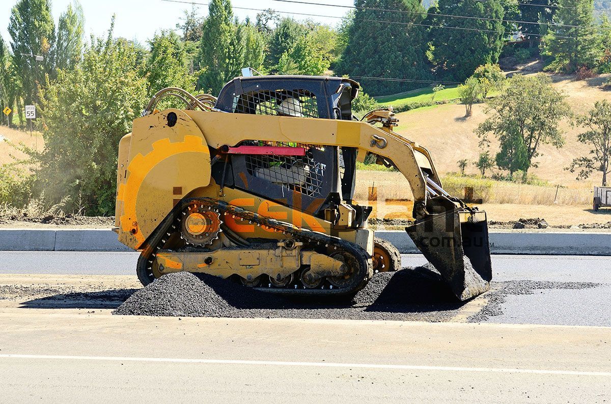 A bulldozer is laying asphalt on the side of a road.