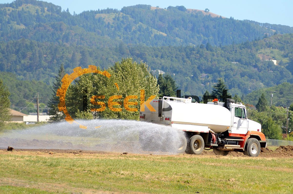 A tanker truck is spraying water on a grassy field