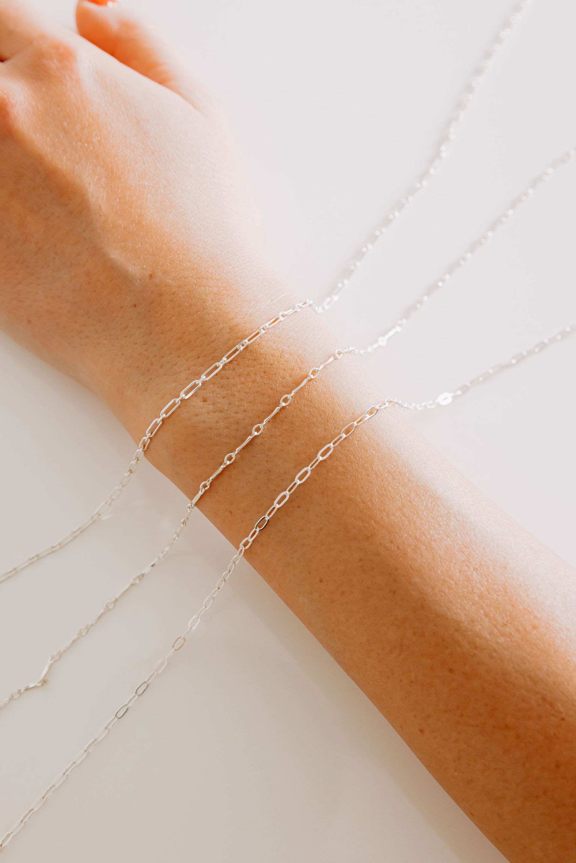 3 silver chain bracelets laying over arm