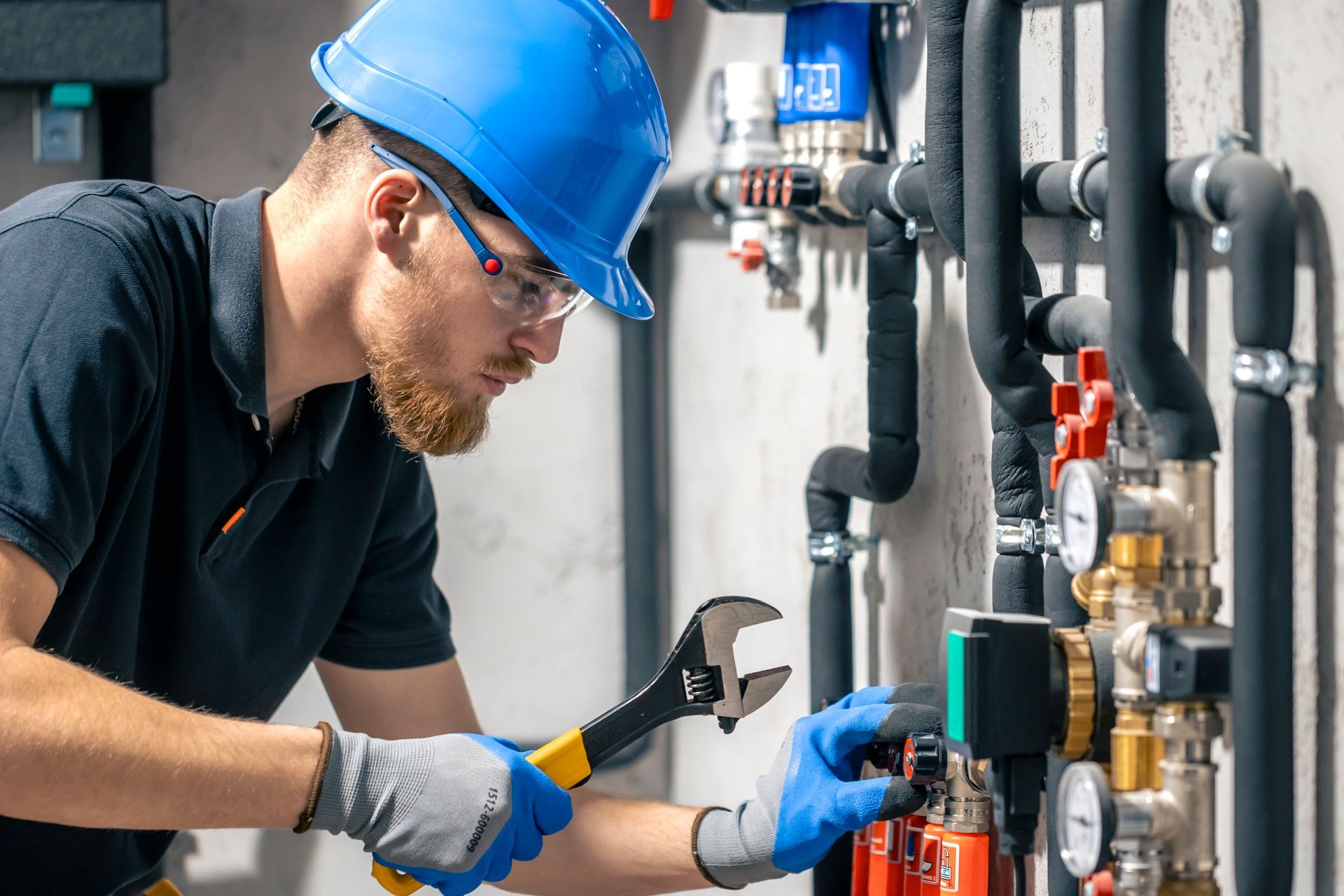 A man wearing a hard hat and safety glasses is working on a pipe with a wrench.