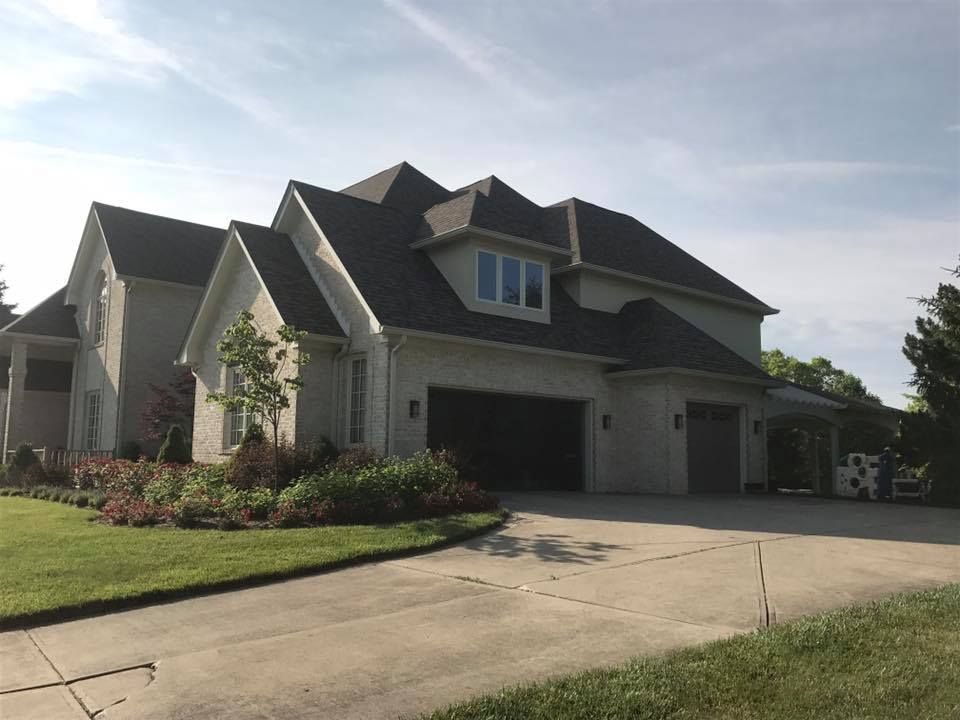 Large two-story house with light-colored siding, dark roof, two-car garage, and green lawn.