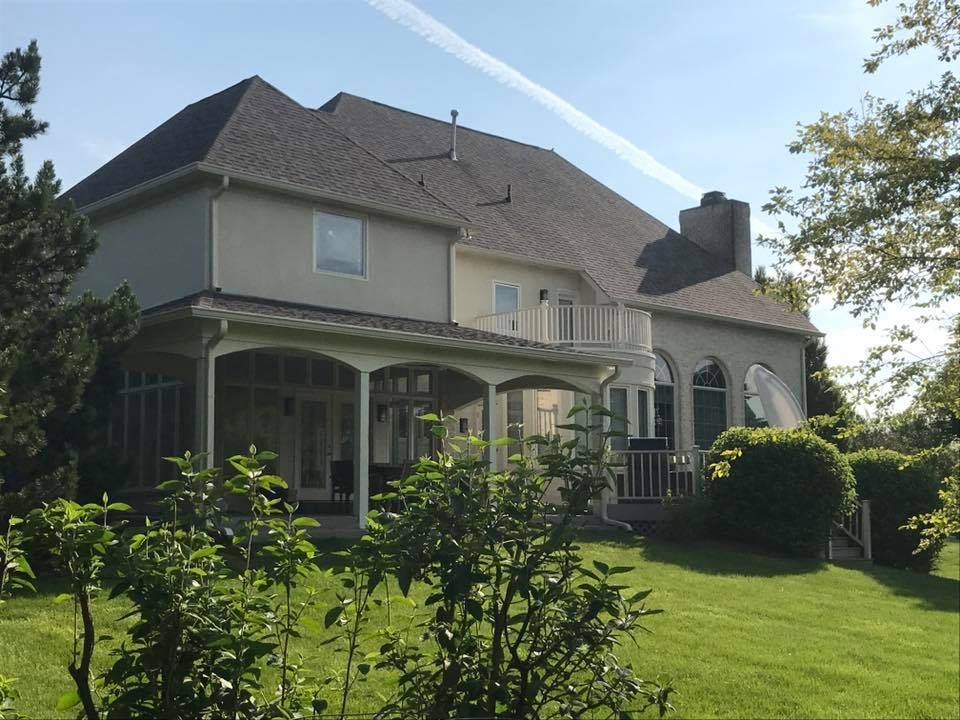 Back exterior of a large two-story house with a covered porch and balcony, set on a green lawn.