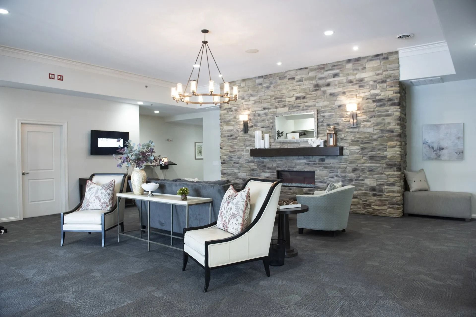 Lounge area with stone fireplace, chandelier, gray furniture, and modern decor.