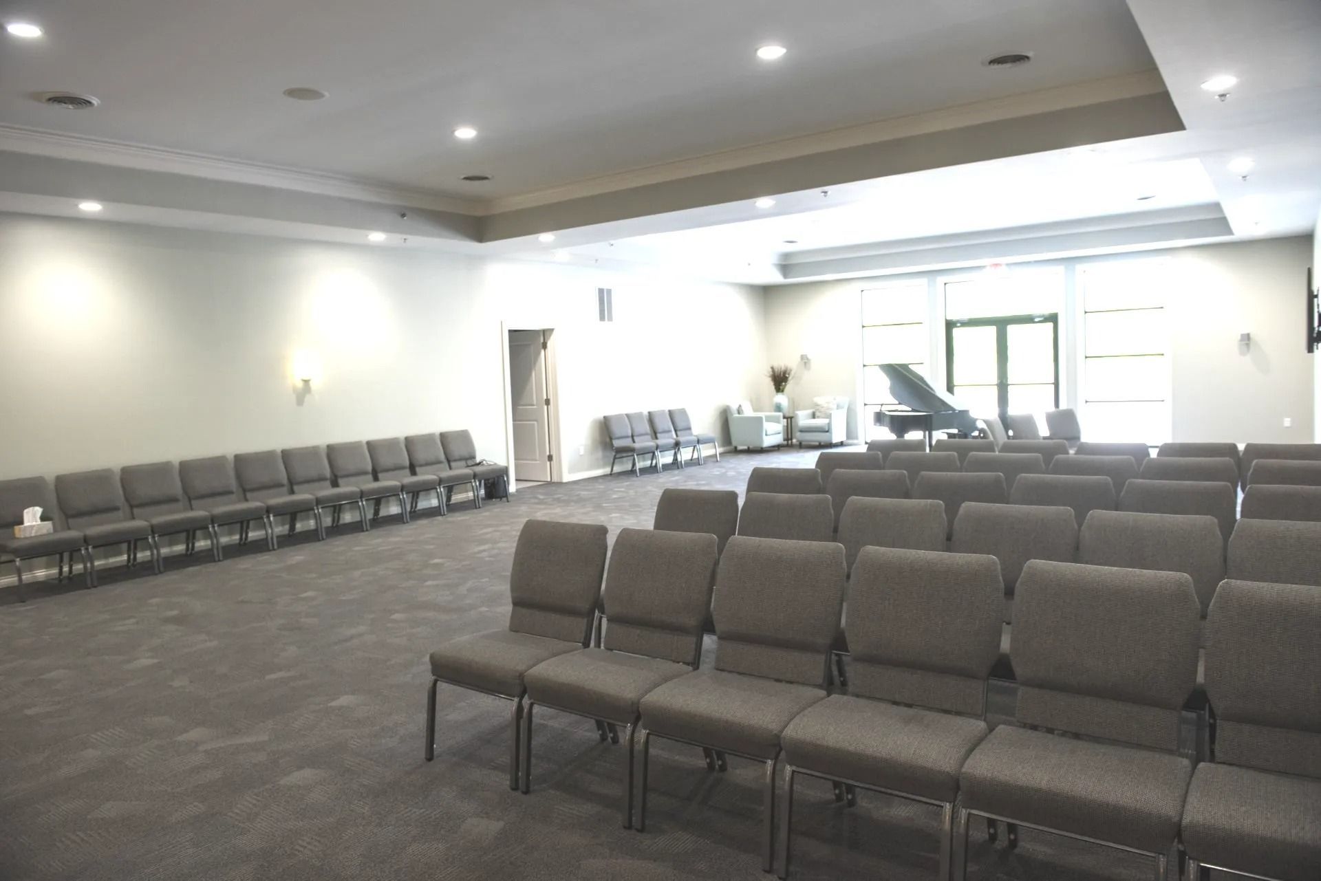 Rows of gray chairs in a large room with a piano, likely a chapel or auditorium.