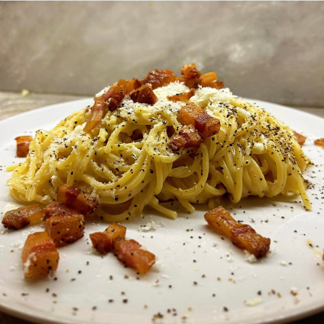 Spaghetti carbonara: pasta with bacon, Parmesan cheese, and black pepper on a white plate.
