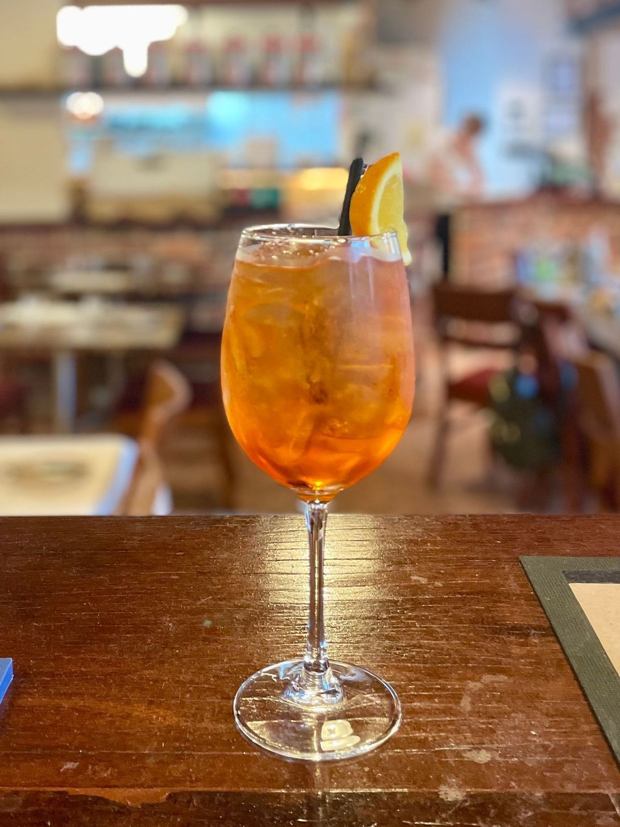 Cocktail in a wine glass with an orange slice on a wooden table in a restaurant.