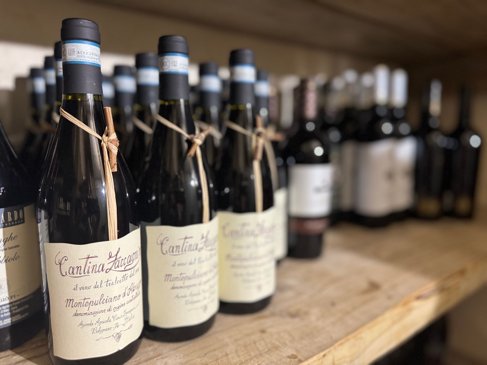 Bottles of red wine in a wooden cellar, some with handwritten labels tied with twine.