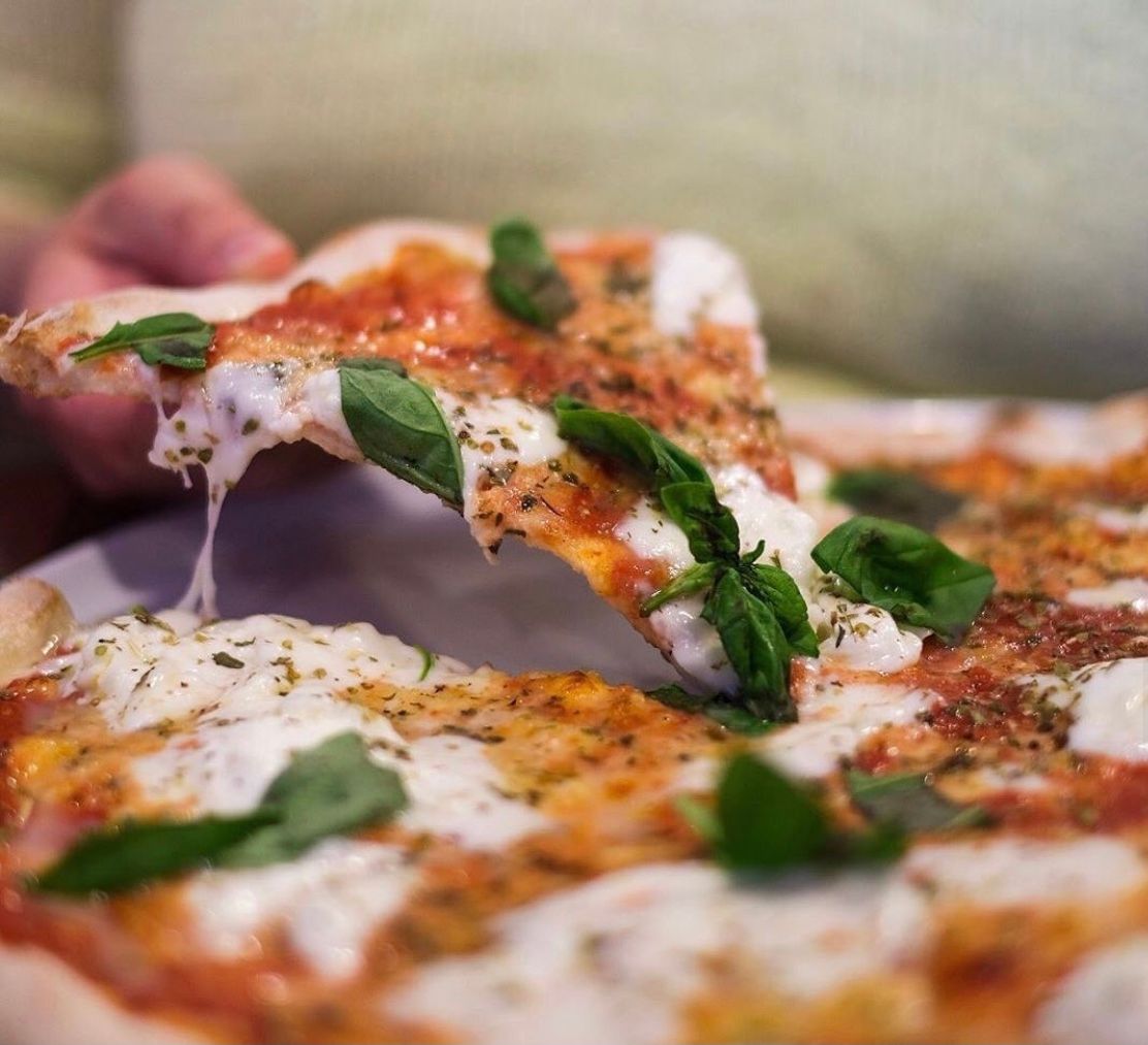 Person lifting a slice of Margherita pizza, cheese stretching; fresh basil, tomatoes.