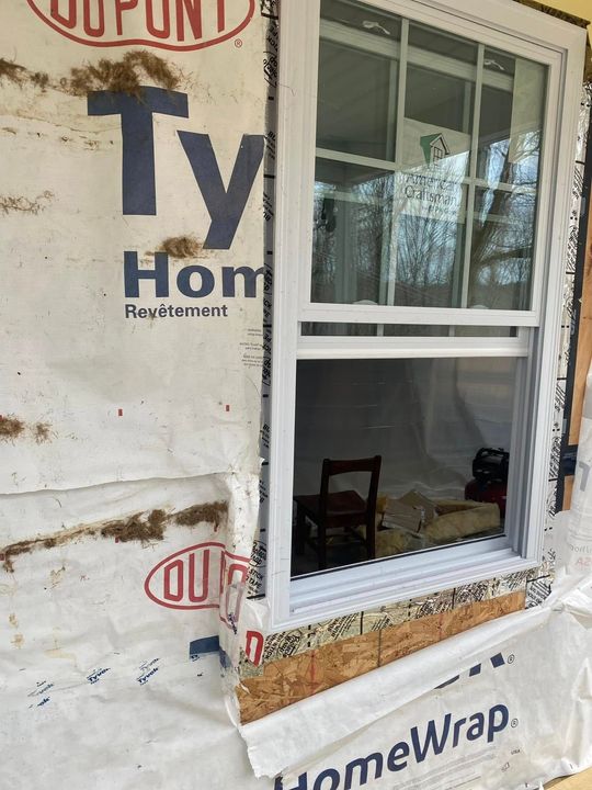 A new white window installed in a wall covered with Tyvek HomeWrap house wrap, showing exposed wooden framing at the sill.