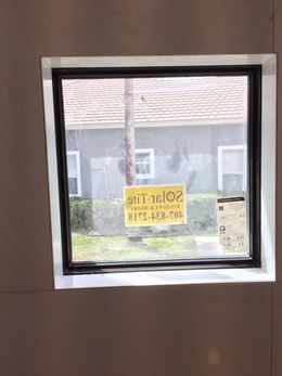 A black-framed window installed in a drywall opening, displaying a Solar-Tite company sticker on the glass.